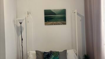 A bedroom with a bed, a painting of a lake, a lamp, and a small table.