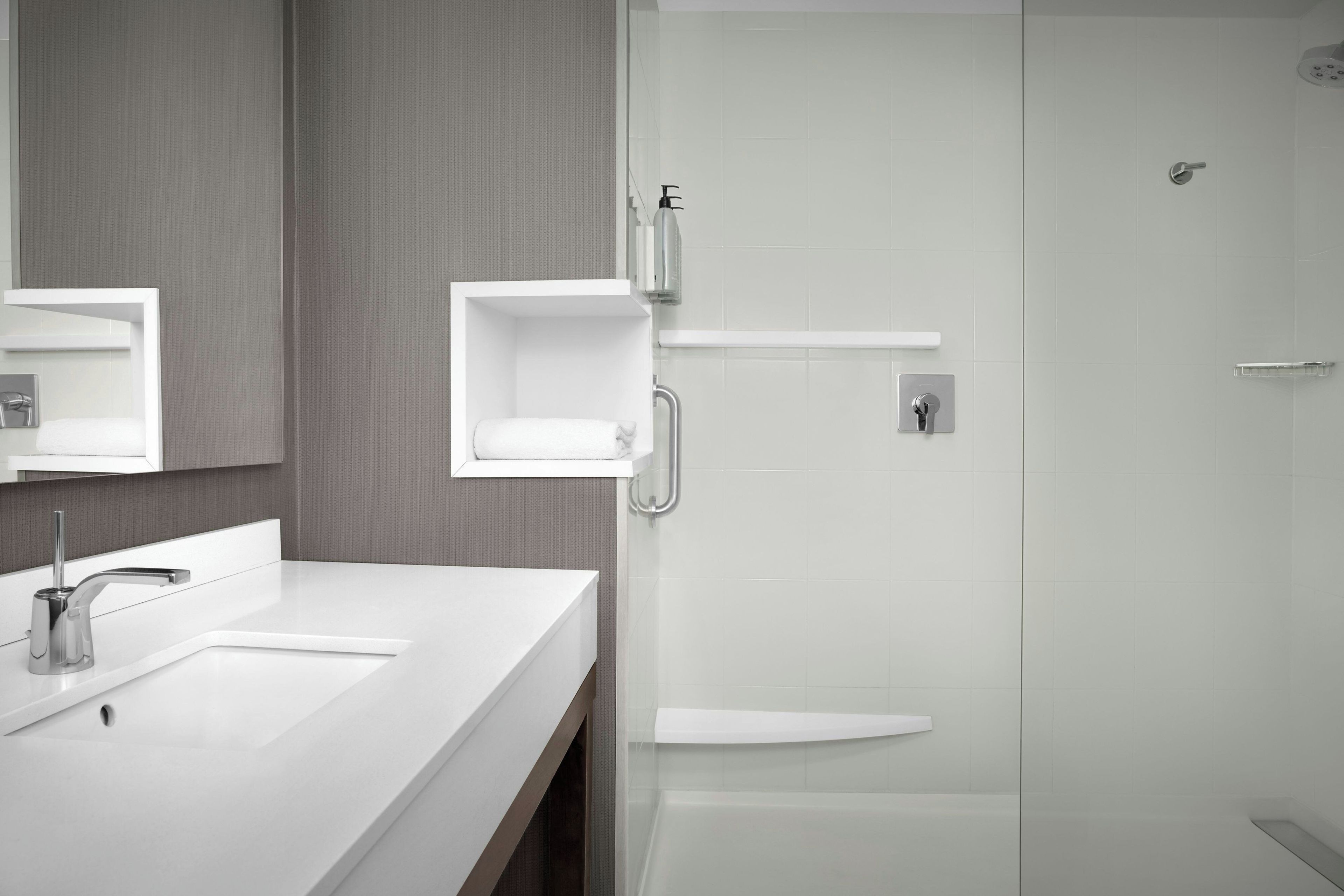 A modern bathroom with a white sink, a mirror, and a shower area.