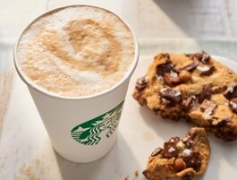 Una taza de Starbucks con un latte, junto a un plato con galletas.