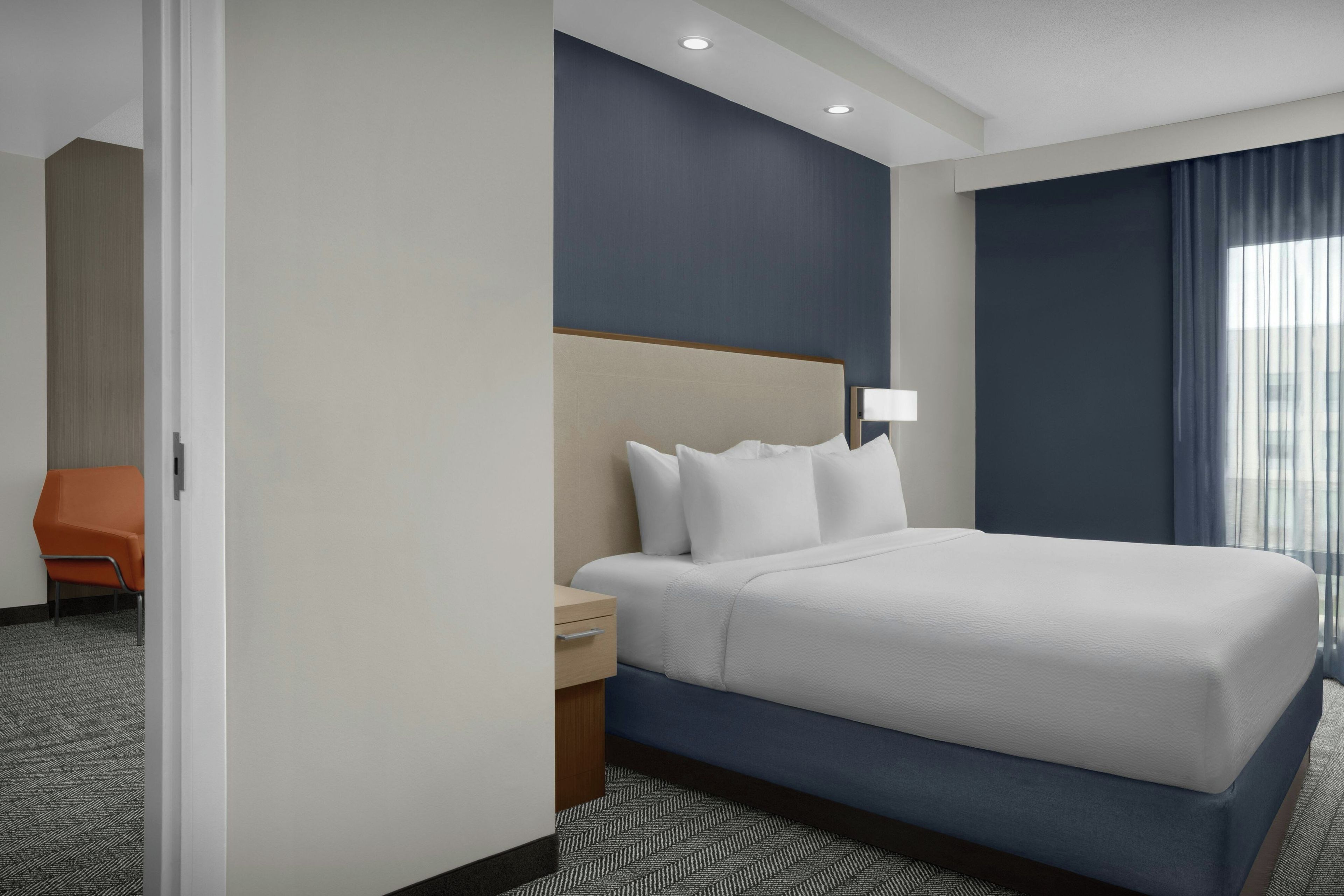 Une chambre d’hôtel avec un grand lit, une table de chevet, une chaise et une fenêtre avec des rideaux.