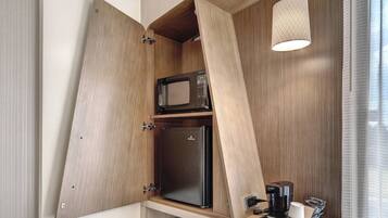 Una kitchenette compacta con microondas, refrigerador y cafetera, que cuenta con muebles de madera y una lámpara colgante.