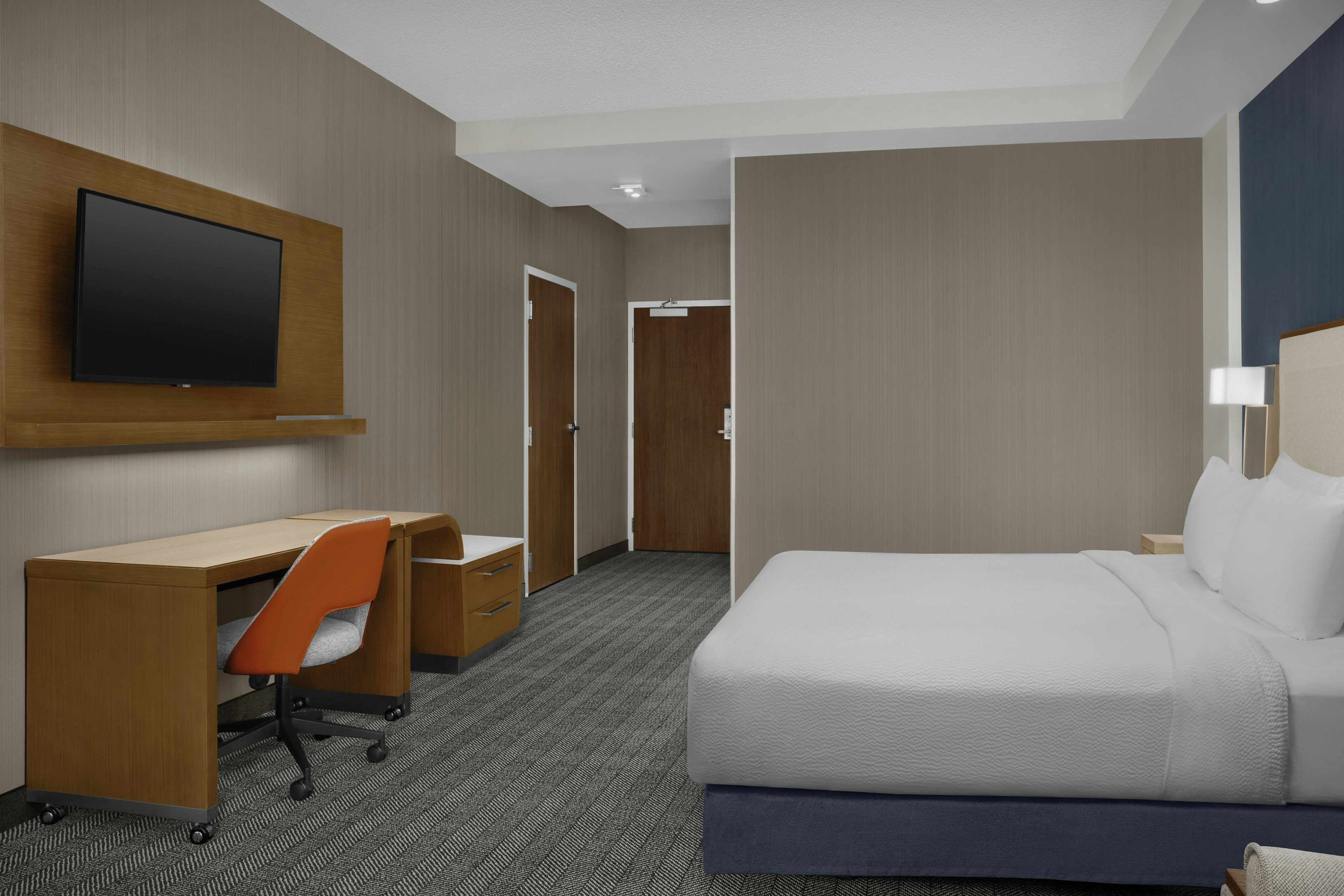 Une chambre d’hôtel avec un lit, un bureau, une chaise, une télévision et une porte.