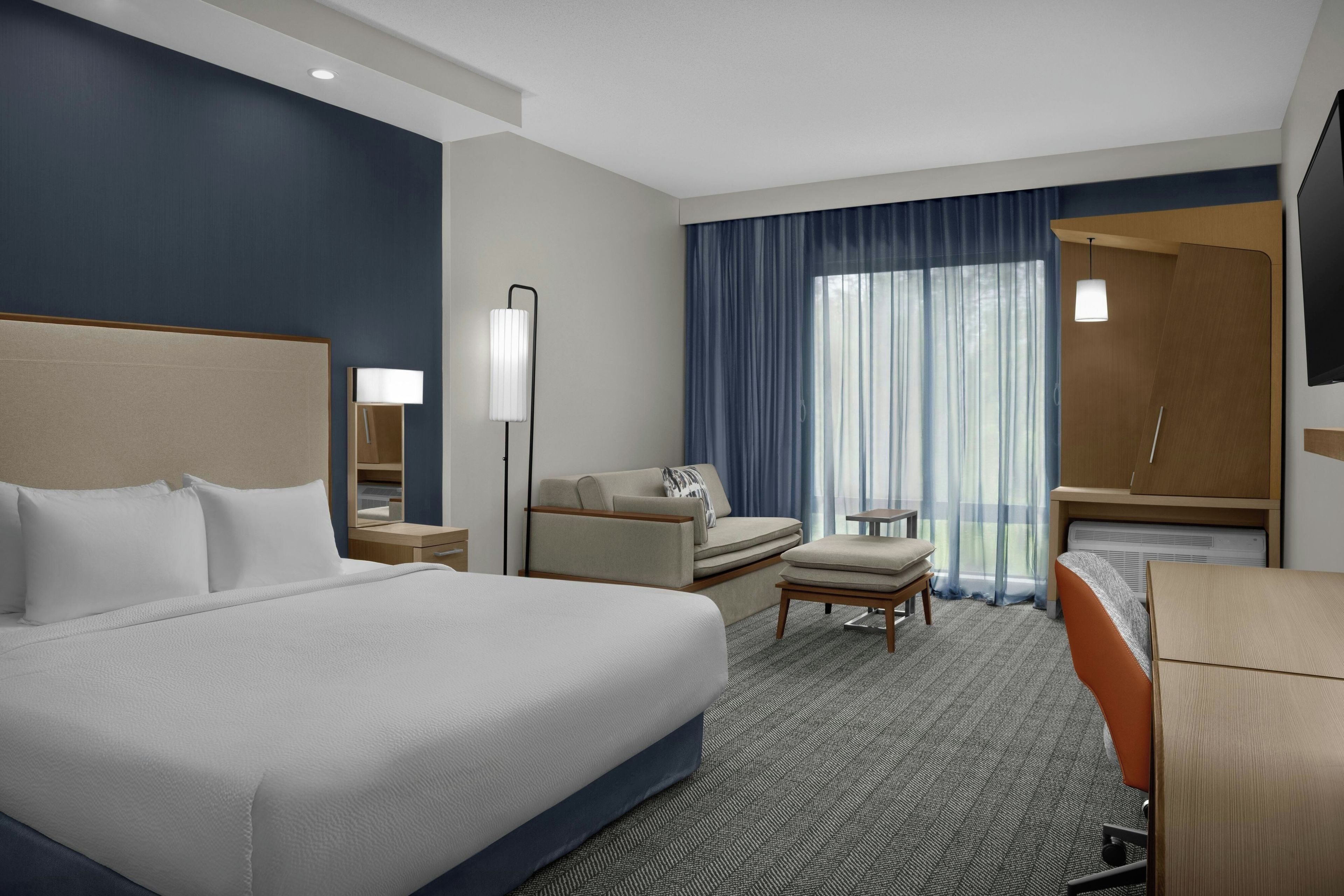A hotel room with a large bed, a desk, a chair, a TV, and a bathroom.