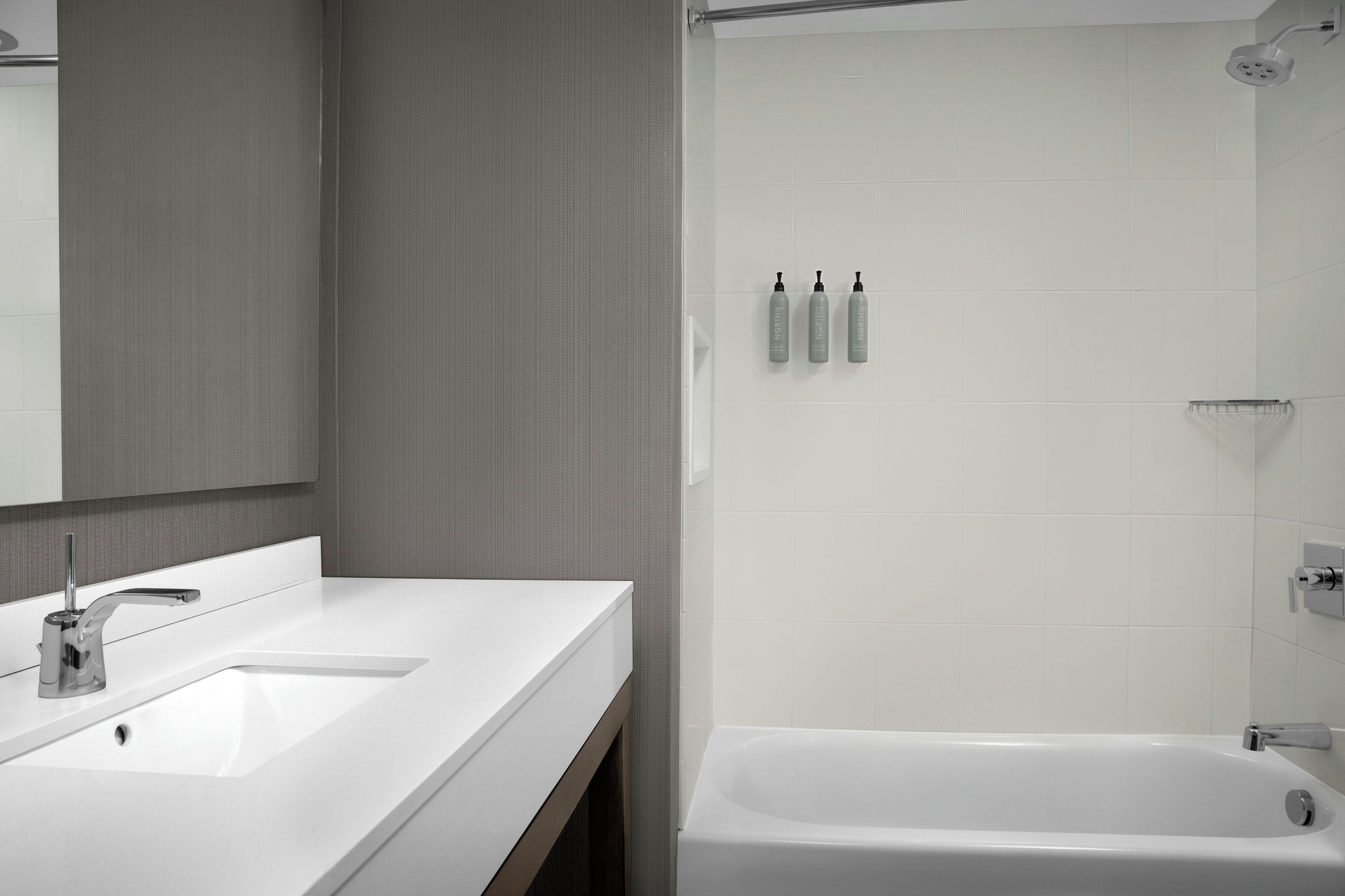 Un baño moderno con un lavabo blanco, un espejo, una ducha con cabezal de ducha manual y artículos de aseo en la pared.