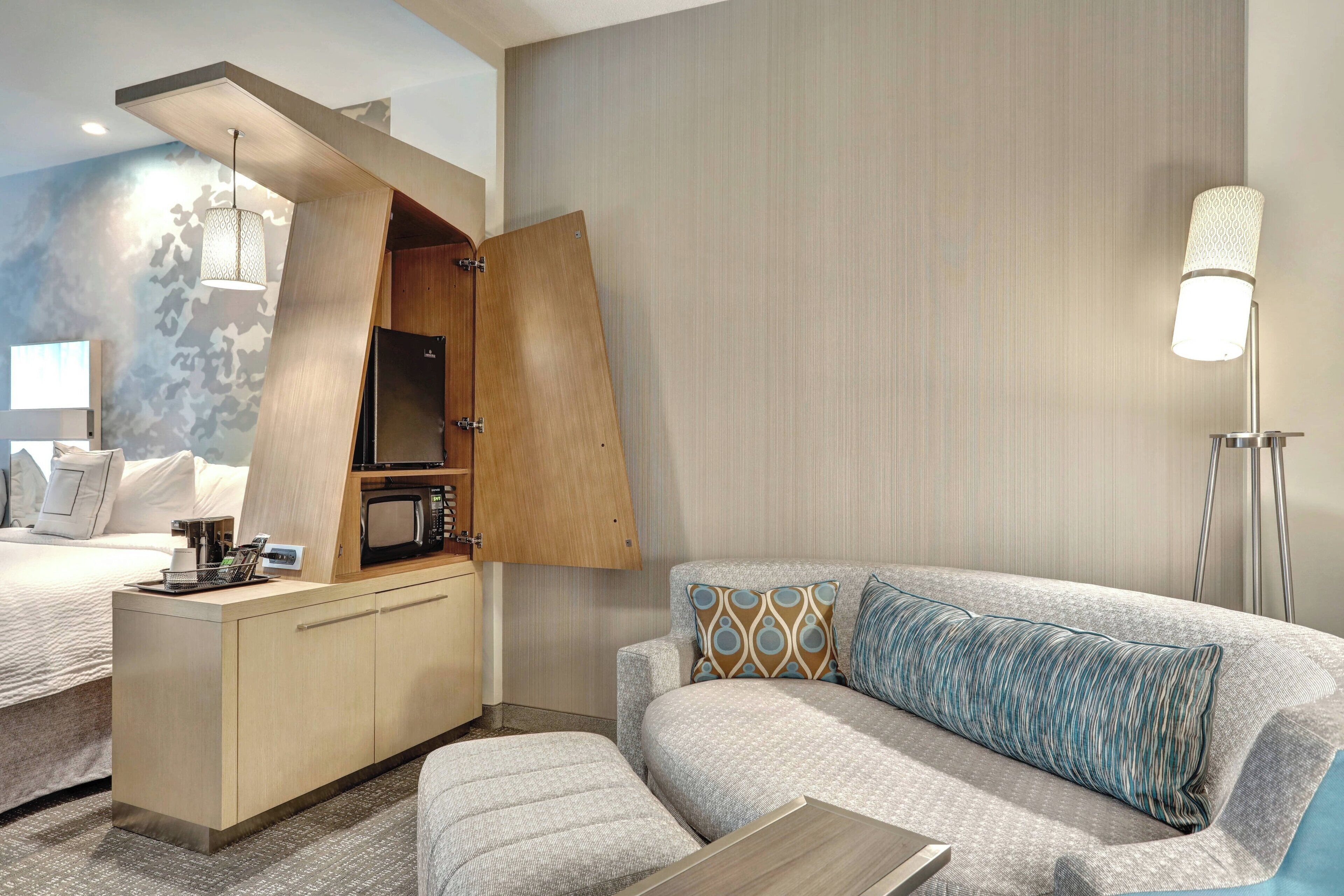 Una habitación de hotel moderna con cama, sofá, una kitchenette pequeña y una lámpara de pie.