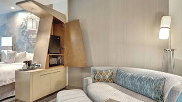 Una habitación de hotel moderna con cama, sofá, una kitchenette pequeña y una lámpara de pie.