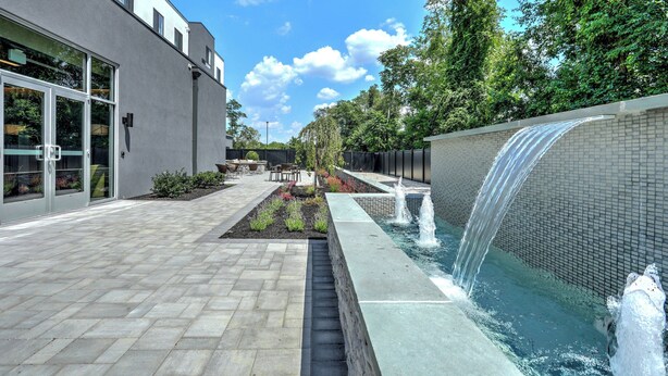 Un edificio moderno con un patio, un pequeño jardín y una fuente de agua.