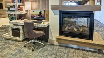 A modern hotel lobby with a reception desk, a computer setup, a fireplace, and a bookshelf.