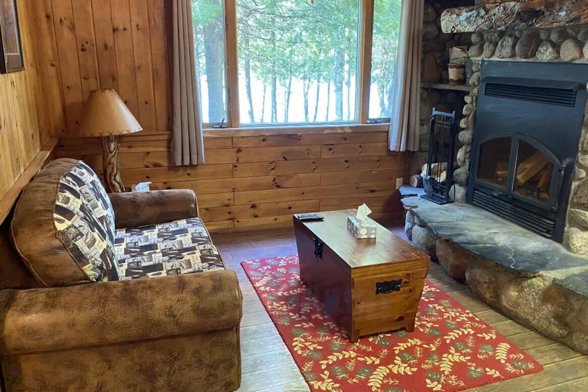 A cozy cabin interior with a wooden sofa, a small wooden table, and a stone fireplace.
