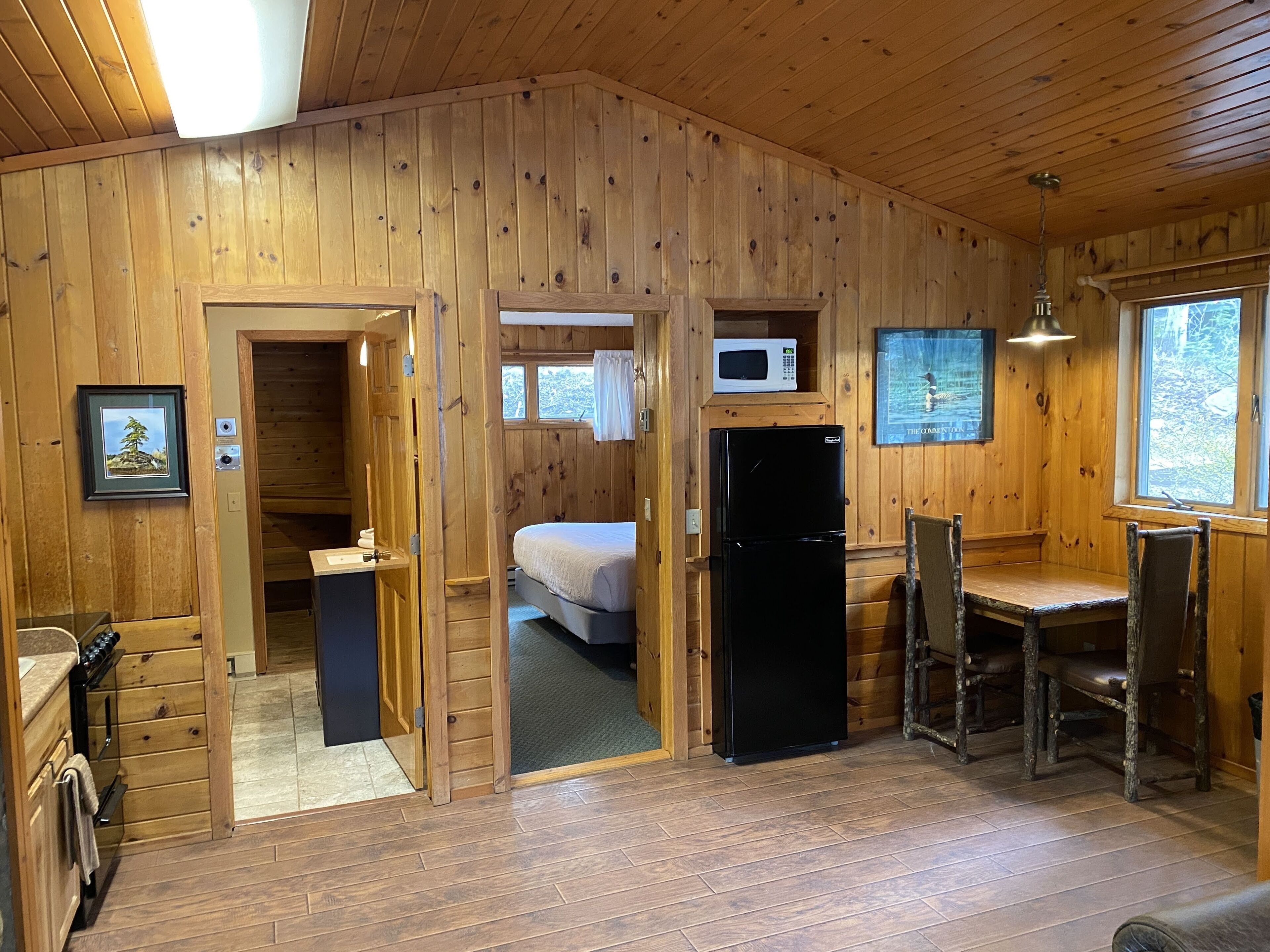 Une cabane en bois comprenant une cuisine, un coin repas et une chambre à coucher.