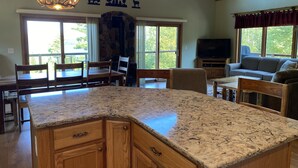 A spacious living area with a large kitchen island, wooden furniture, and a stone fireplace. - Gunflint Lodge & Outfitters (Grand Marais)