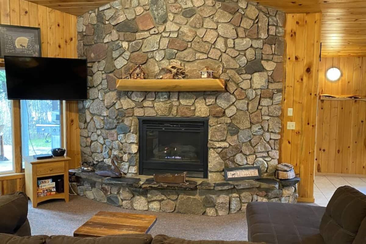 A stone fireplace with a television above it, a wooden shelf, and a cozy seating area with a flat-screen TV.