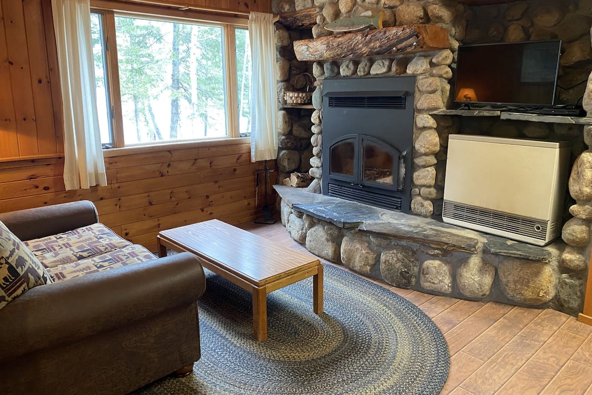 A cozy cabin interior with a stone fireplace, wooden walls, a sofa, and a television.