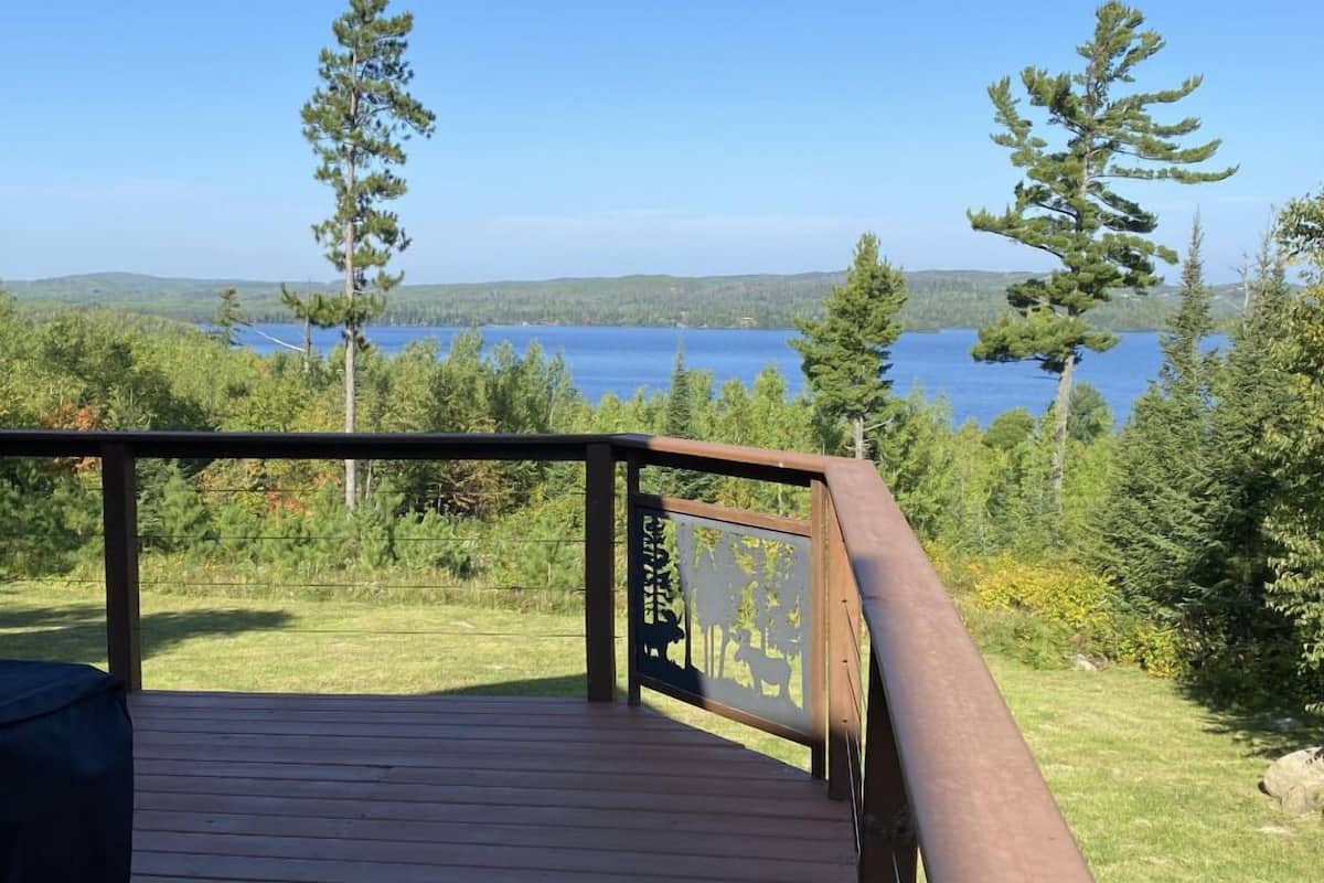 A wooden deck with a metal railing overlooking a lake surrounded by trees.