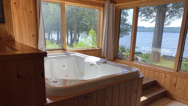 A wooden cabin with a hot tub, large windows, and a view of a lake. - Gunflint Lodge & Outfitters (Grand Marais)