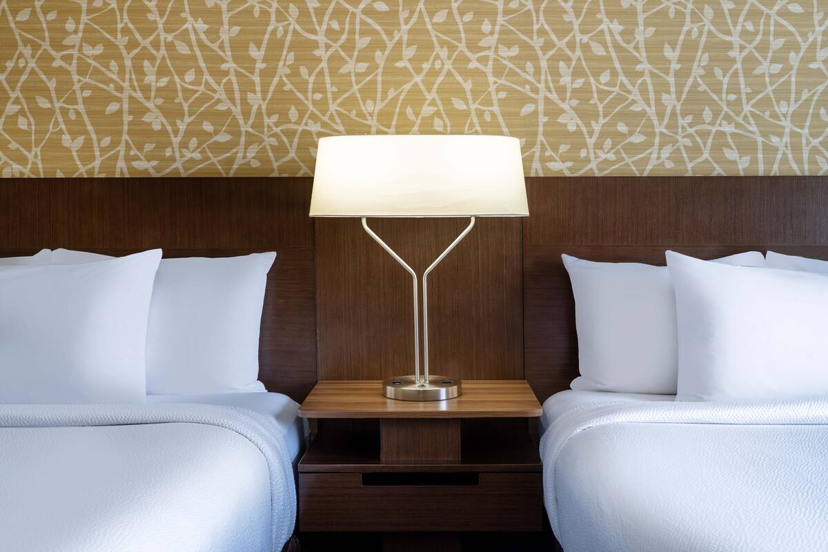 A hotel room with two beds, a nightstand, and a wall with a leaf pattern.