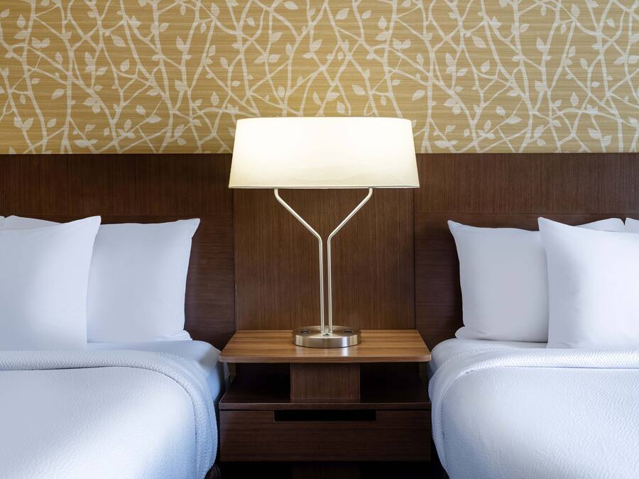 A hotel room with two beds, a nightstand, and a wall with a leaf pattern.