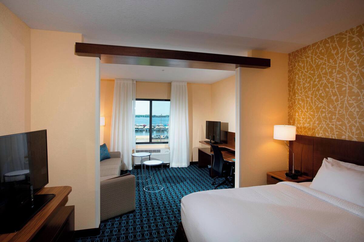 A hotel room with a bed, a desk, a TV, a chair, and a view of the sea.