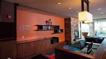 Een moderne lounge met een 'Connect & Print'-bord, een open haard, comfortabele zitplaatsen en een groot raam met uitzicht.