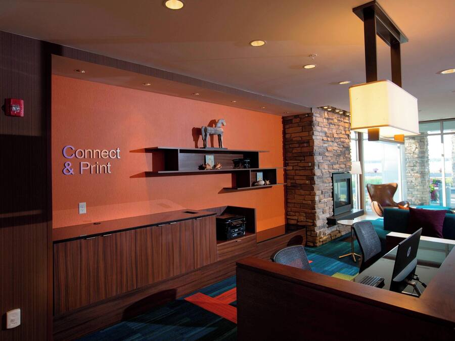 Een moderne lounge met een 'Connect & Print'-bord, een open haard, comfortabele zitplaatsen en een groot raam met uitzicht.