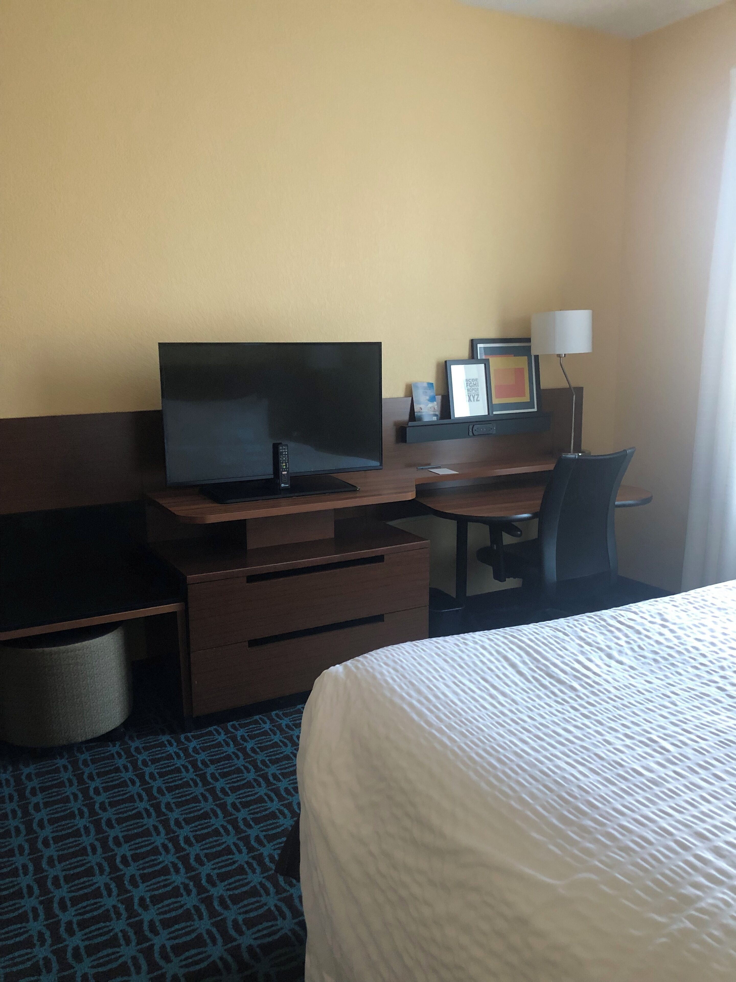 Una habitación de hotel con cama, escritorio, computadora, televisor y lámpara.