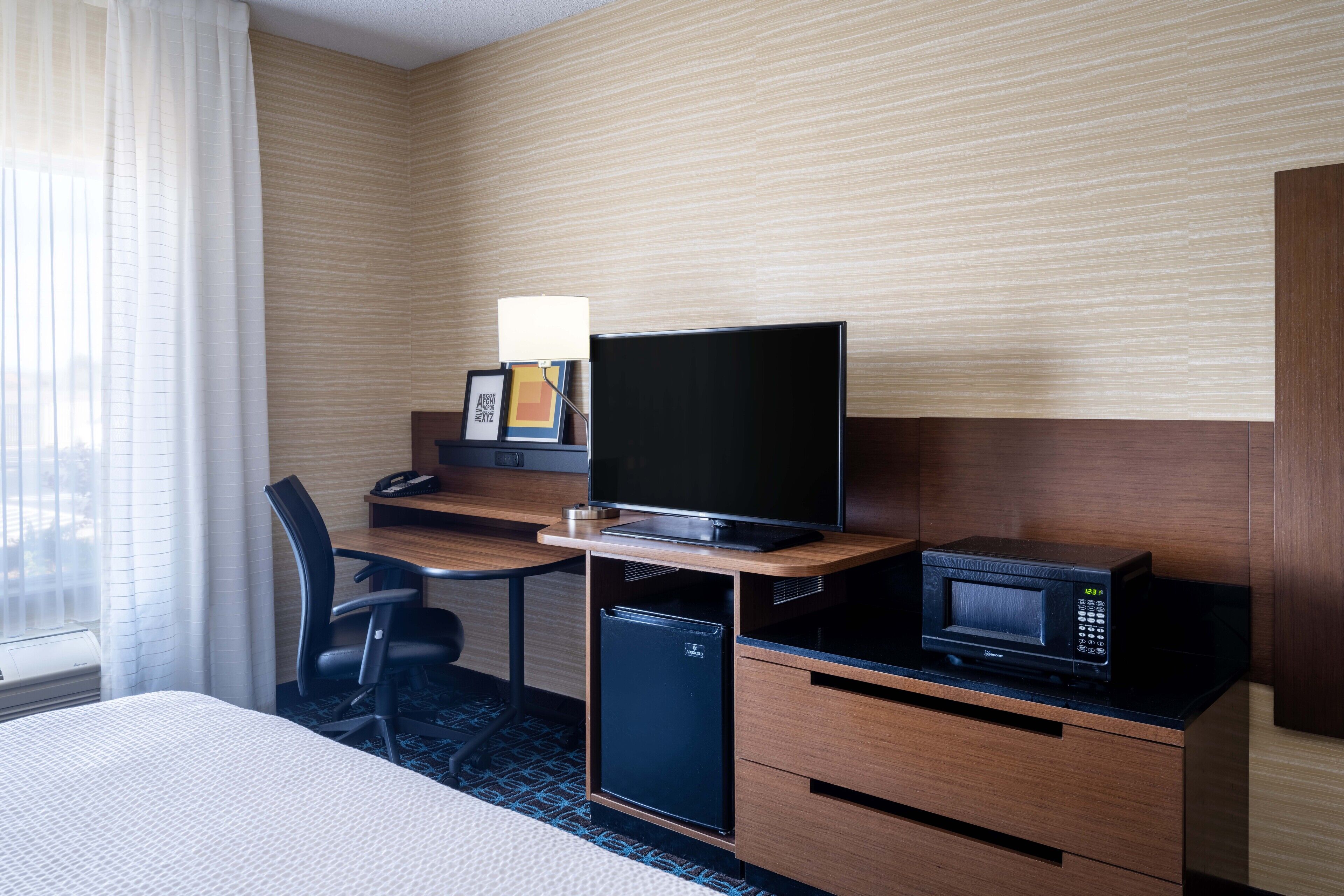 A hotel room with a bed, a desk with a computer, a TV, a microwave, and a small refrigerator.