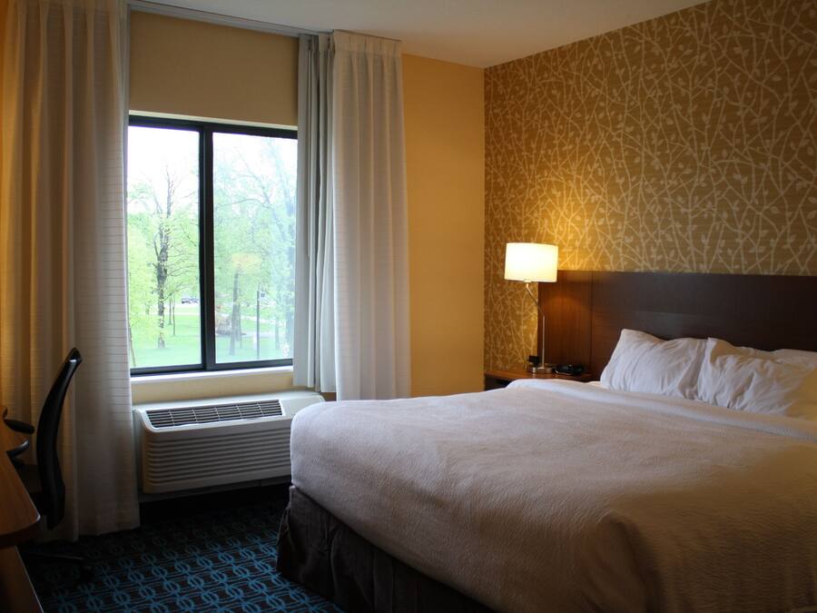 Ein Hotelzimmer mit einem großen Bett, einem Schreibtisch, einem Sessel, einem Fenster mit Vorhängen, einer Wandheizung und einem Wandpapier mit Muster.