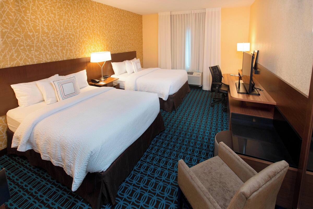 A hotel room with two beds, a desk, a chair, and a TV.