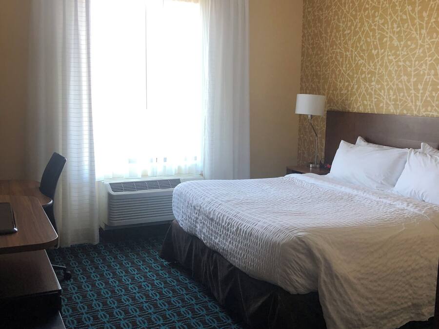 Een hotelkamer met een bed, een bureau, een lamp en een raam met gordijnen.