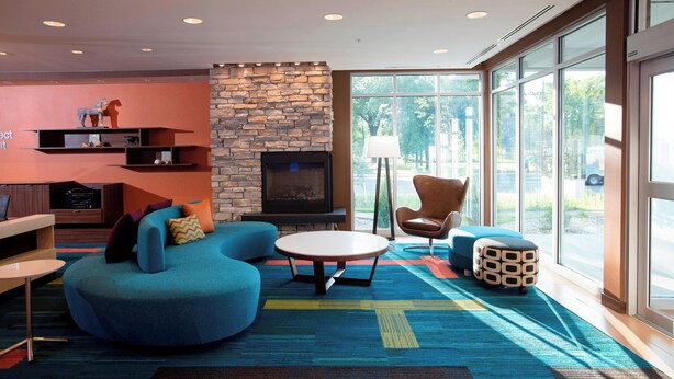 A modern living room with a stone fireplace, a blue sofa, a round coffee table, and a large window offering a view of the outdoors. - Fairfield Inn & Suites by Marriott Detroit Lakes (Detroit Lakes)