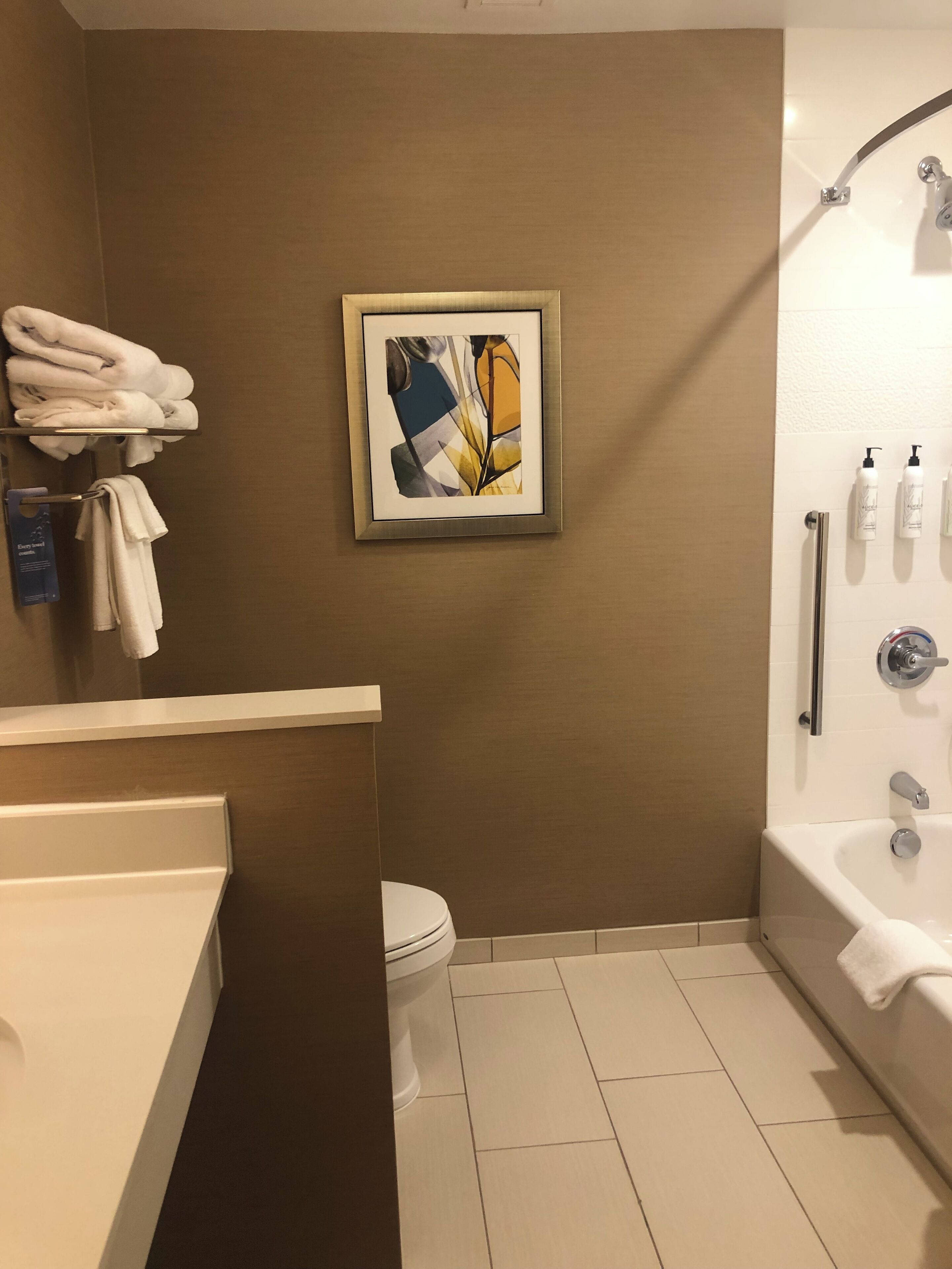 A bathroom with a toilet, a bathtub, and a shower. There is a towel rack with towels and a framed picture on the wall.