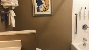 A bathroom with a toilet, a bathtub, and a shower. There is a towel rack with towels and a framed picture on the wall.