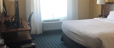 A hotel room with a bed, desk, and air conditioning unit.