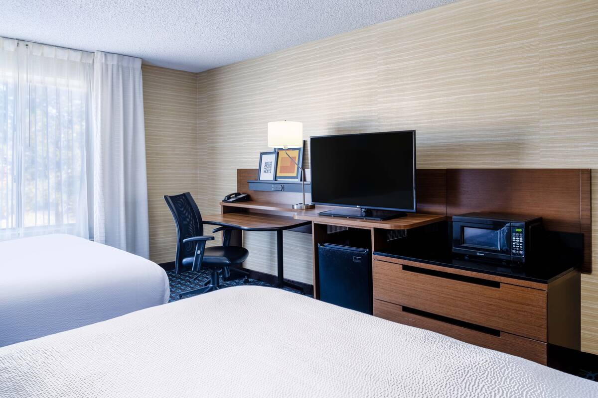 A hotel room with two beds, a desk with a TV, a microwave, and a small fridge.