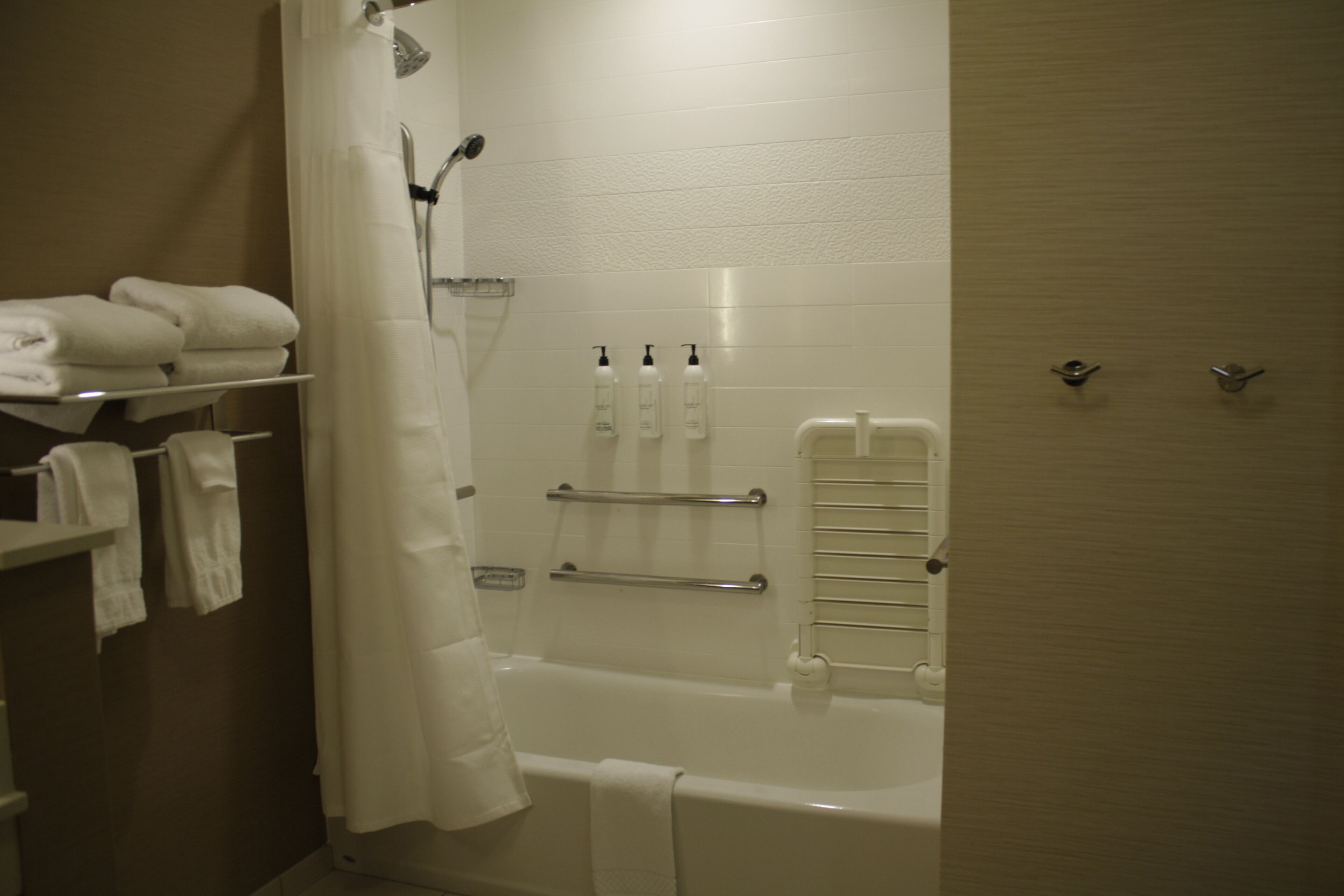 A bathroom with a bathtub, a shower curtain, a towel rack, and a shelf with towels.