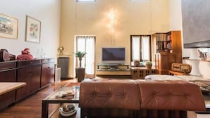 A spacious living room with a large window, a television, a bookshelf, and a leather sofa.