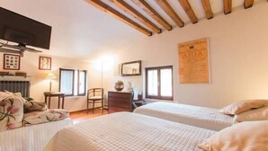 A bedroom with two beds, wooden beams on the ceiling, a TV, and framed pictures on the wall.