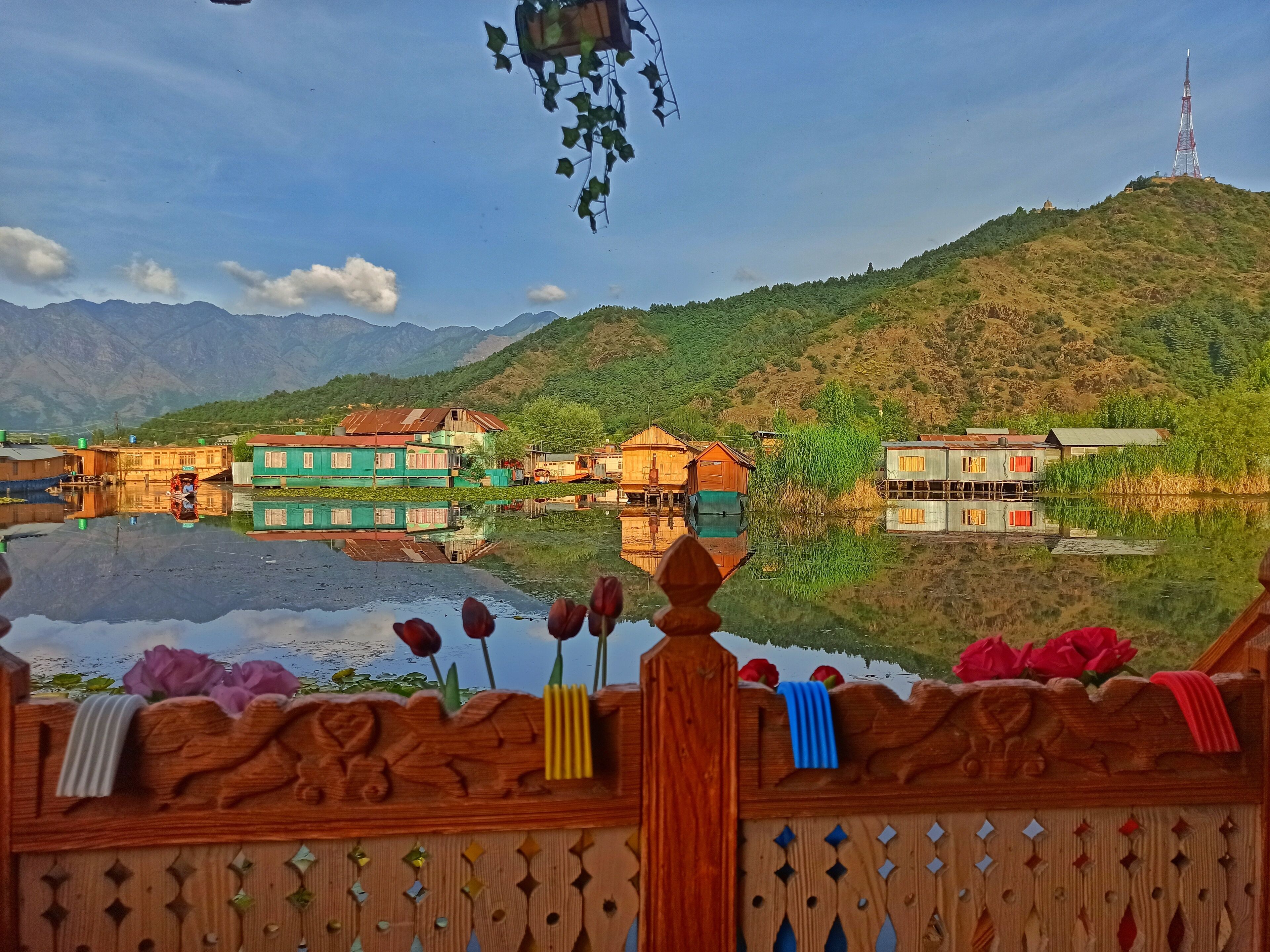 A riverside village with traditional houses, a mountain backdrop, and a prominent communication tower.