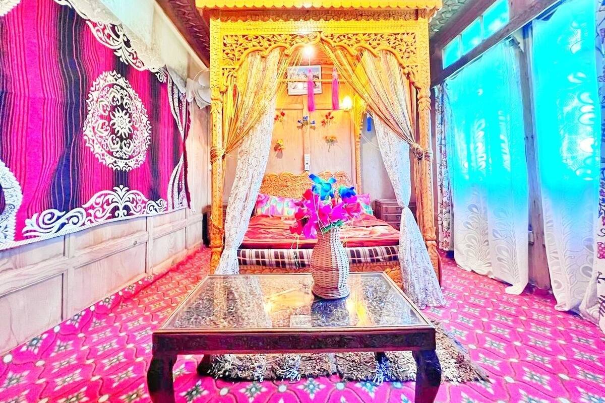 A room with a canopy bed, a glass coffee table, patterned curtains, and a decorative wall tapestry.