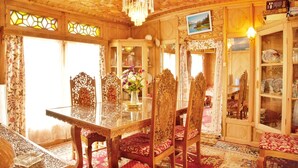 Uma sala de jantar com mesa de vidro, cadeiras ornamentadas e um lustre.