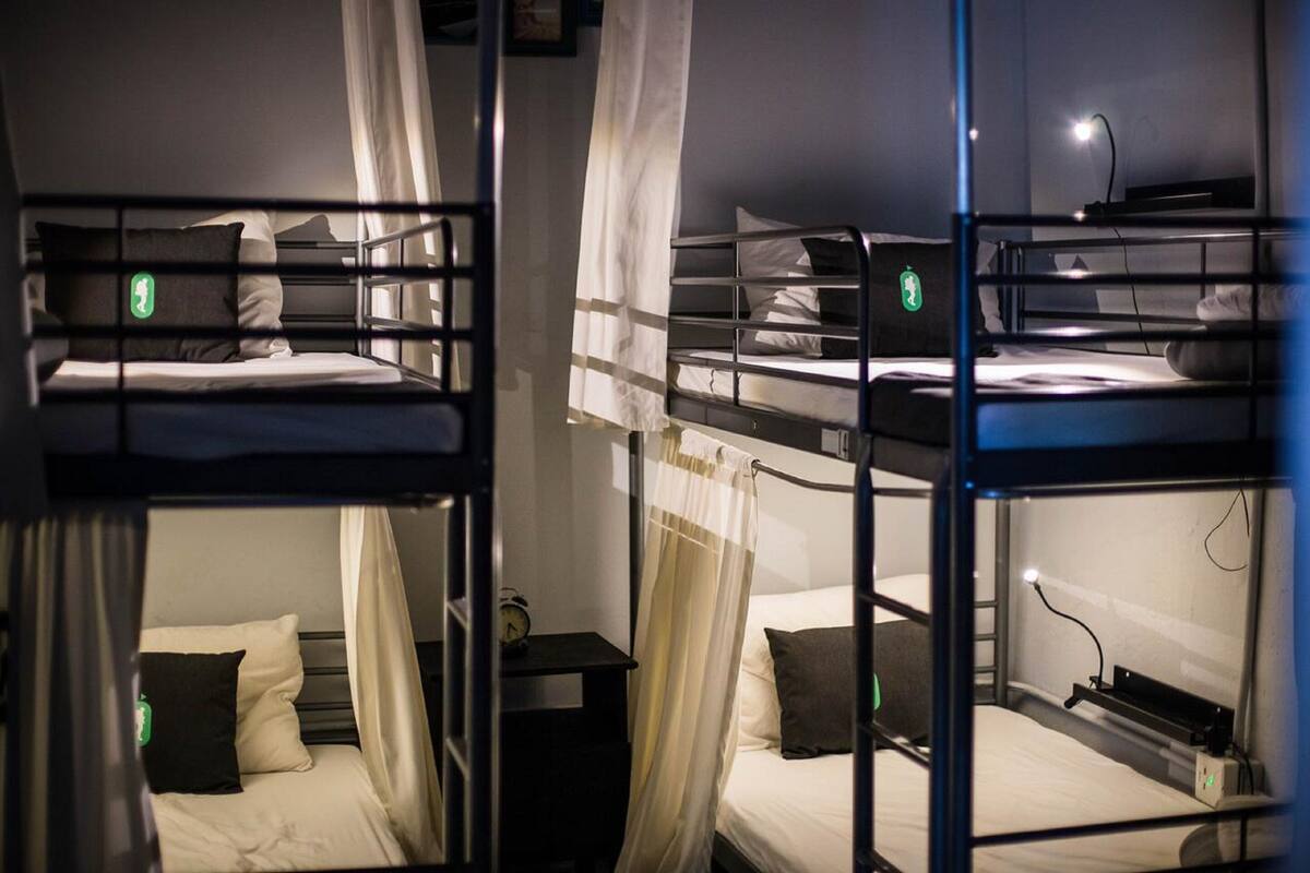 A room with bunk beds, a small bedside table with a lamp, and a curtain.