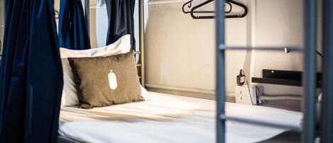 A bunk bed with a hanging garment rack and a small desk with a computer.