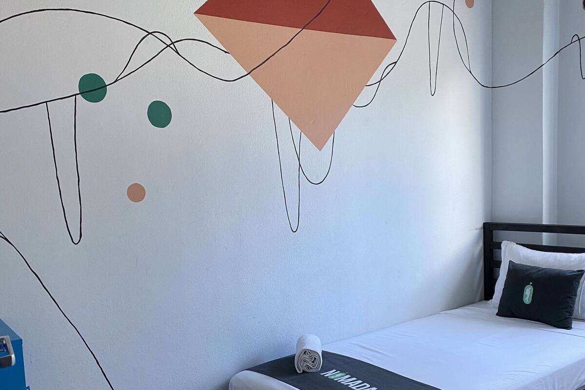 A bedroom with a bed, a wall with abstract art, and a wooden chair.
