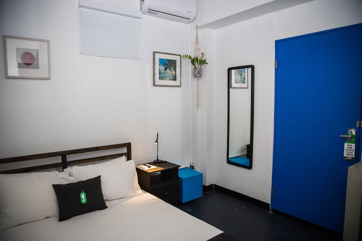 A hotel room with a bed, a nightstand, a blue cabinet, a wall-mounted mirror, and a blue door.