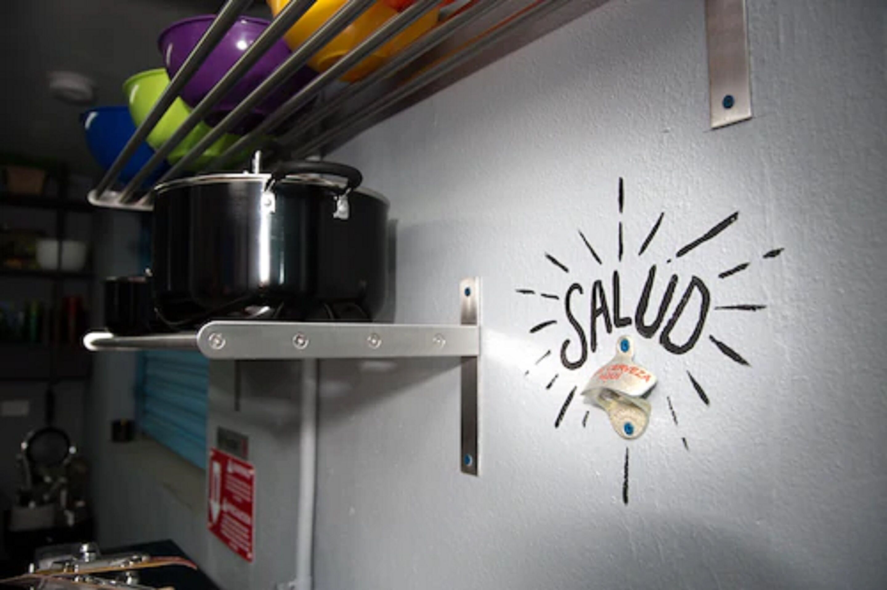Una cocina con ollas en un estante y una pared con la palabra 'SALUD' y una pegatina.