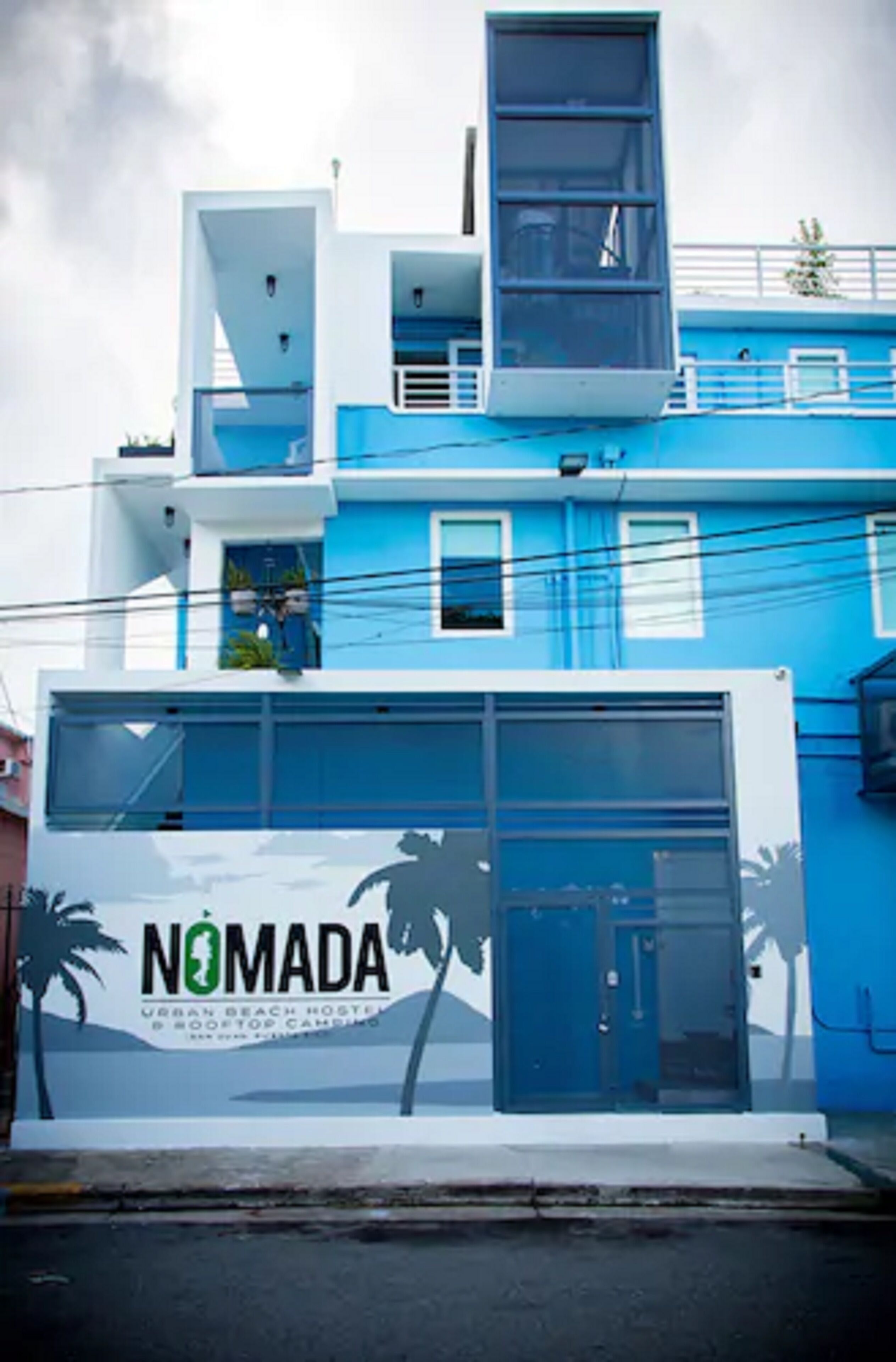 A modern building with a sign reading "NOMADA Urban Beach Hostel & Rooftop Camping."