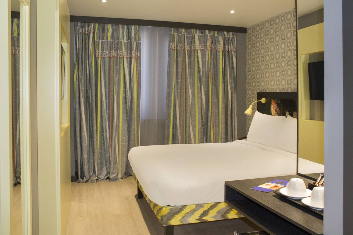 A hotel room with a large bed, a bedside table with a lamp, and a mirror.