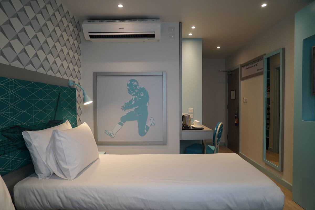 A modern hotel room with a large bed, a desk, and a wall-mounted air conditioner.