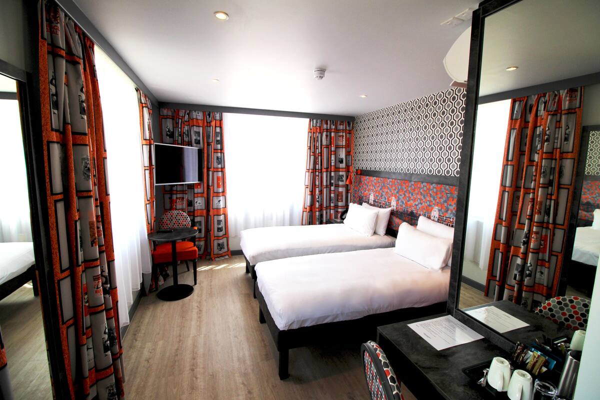 A hotel room with two beds, a desk with a mirror, a TV, and a patterned wall.