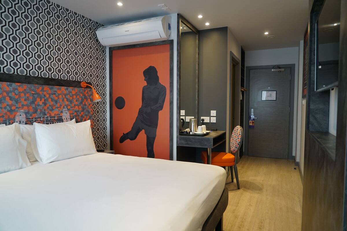 A hotel room with a bed, a desk, a chair, and a wall with a geometric pattern.
